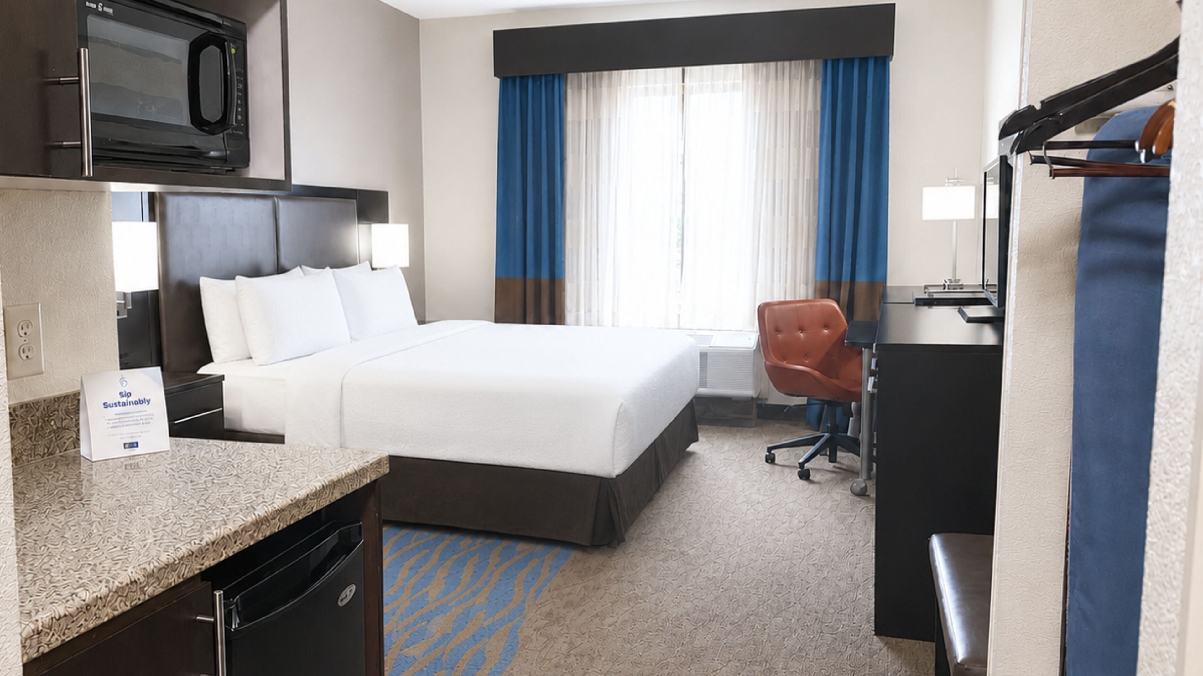 Ein Hotelzimmer mit Bett, Schreibtisch, Stuhl, Mikrowelle und einem Hinweis auf Nachhaltigkeit.