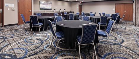 A conference room with round tables and blue patterned chairs, carpeted floor, and a painting on the wall.
