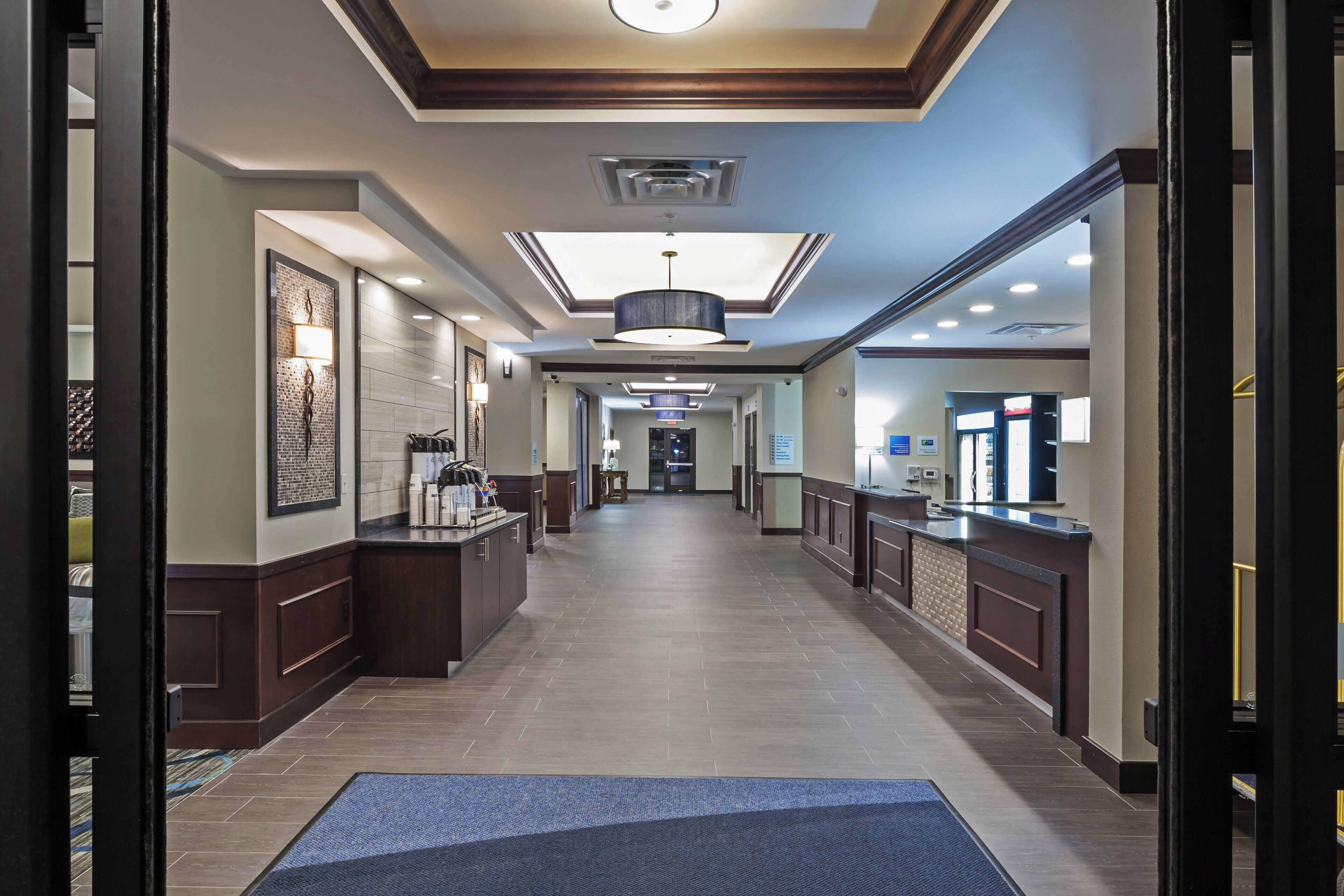 A hotel lobby with a reception desk, a waiting area, and a hallway leading to the entrance.