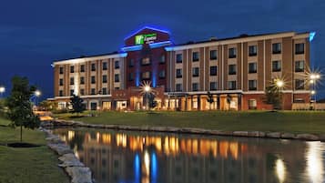 Een Holiday Inn Express & Suites hotel, weerspiegeld in het water, omgeven door een verzorgd gazon en een stenen rand.