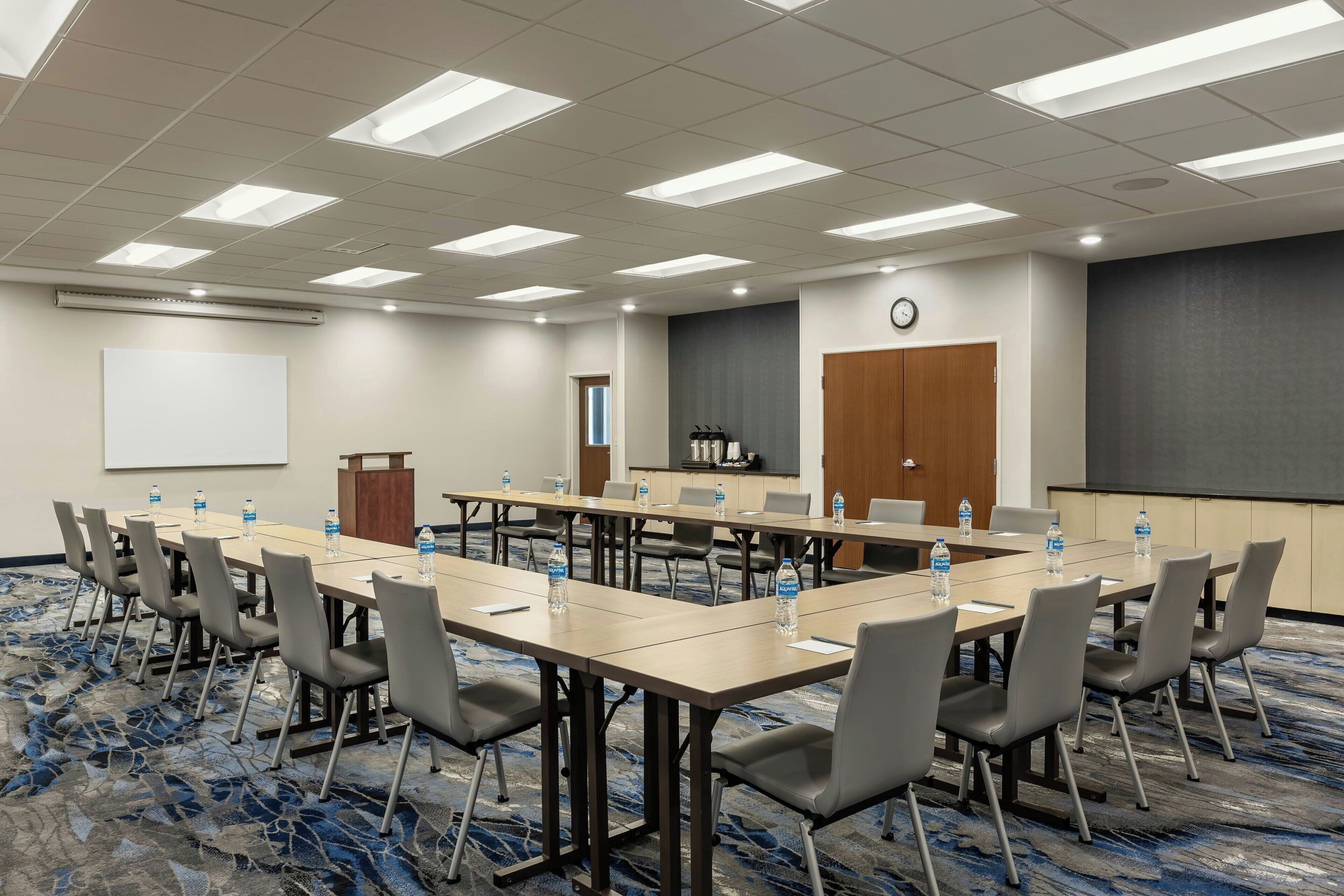 A conference room with a long table, chairs, a projector screen, and a clock on the wall.