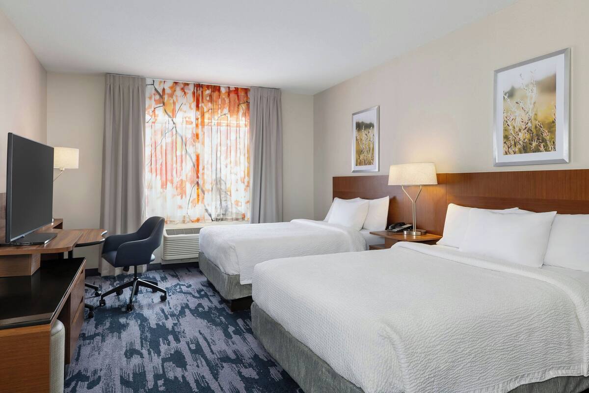 Une chambre d’hôtel avec deux lits, un bureau, une télévision et une fenêtre avec des rideaux.