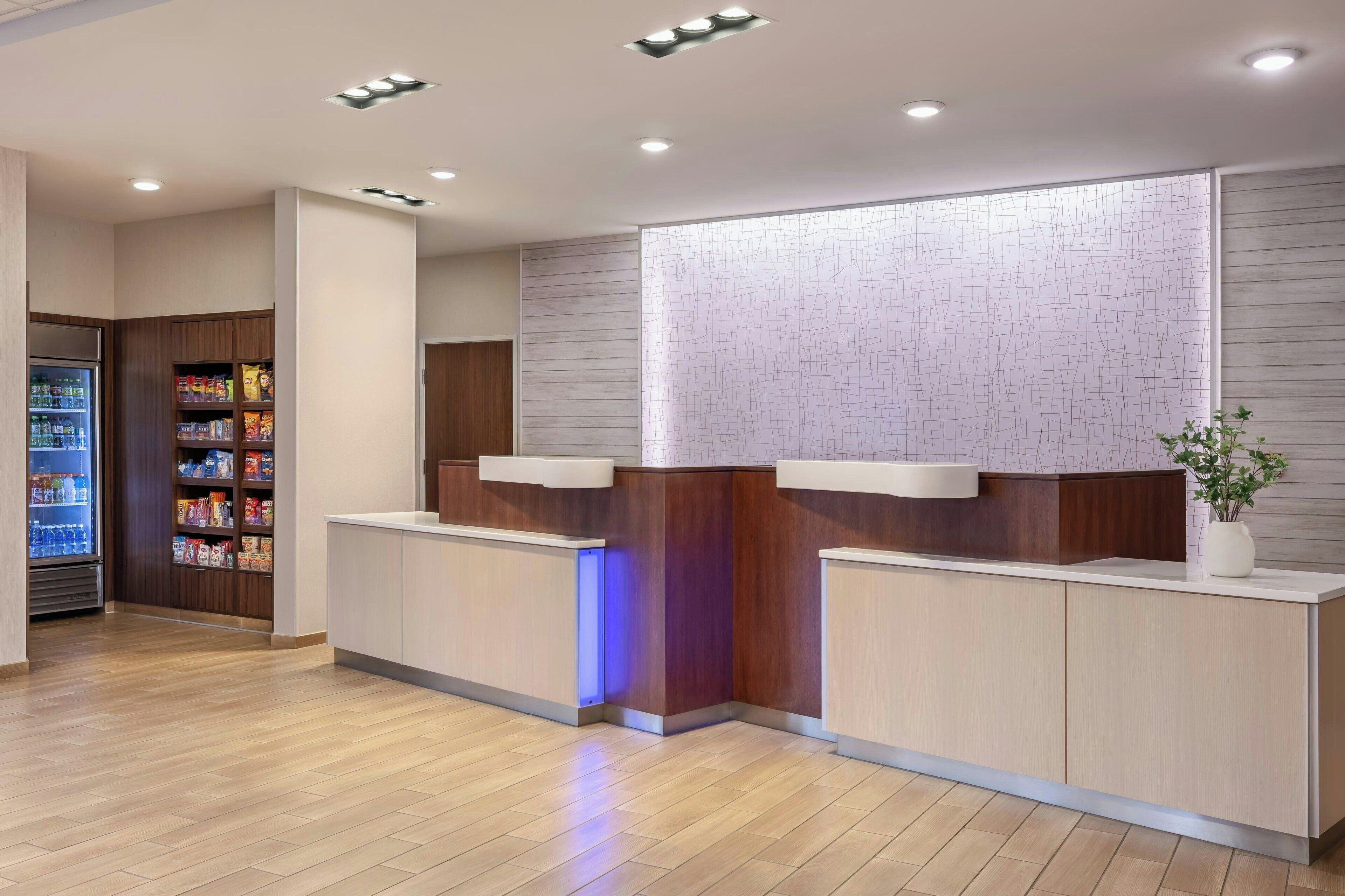 A reception area with a wooden reception desk, a refrigerator stocked with beverages, and a wall-mounted display.