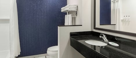 Une salle de bain moderne avec un mur d’accent bleu, des toilettes blanches, un lavabo noir et un miroir placé au-dessus.