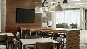 Een moderne hotellobby met een houten accentmuur, een flatscreen-tv, een bar en een zithoek met tafels en stoelen.