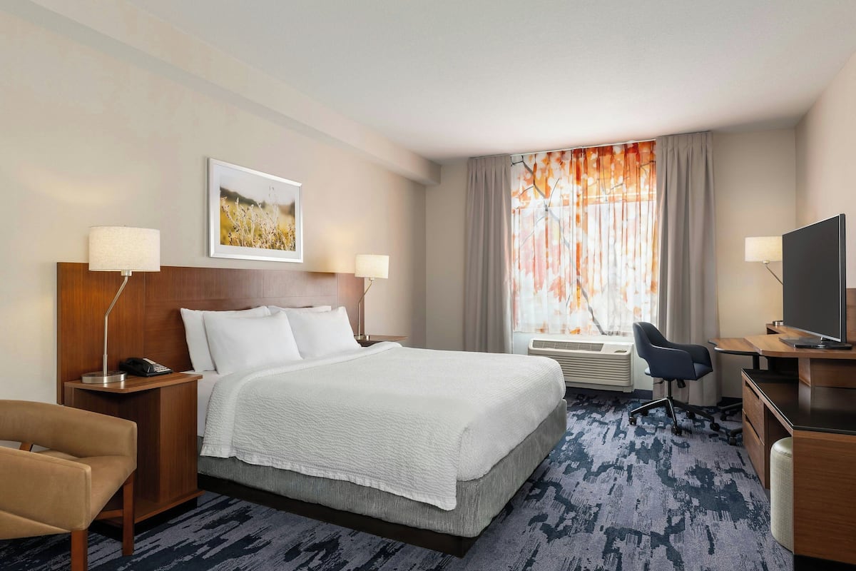Une chambre d’hôtel avec un grand lit, un bureau avec une chaise, une télévision et une fenêtre avec des rideaux.