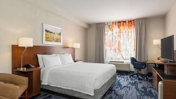 A hotel room with a large bed, a desk with a chair, a television, and a window with curtains.