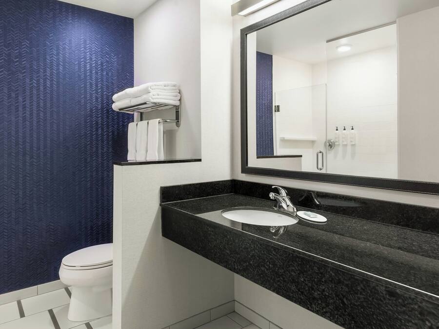 Un baño moderno con inodoro blanco, lavabo de granito negro y un espejo grande.
