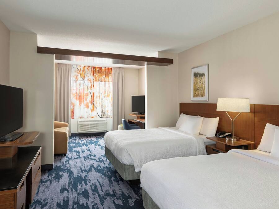 Una habitación de hotel con dos camas, televisión, escritorio y una silla.