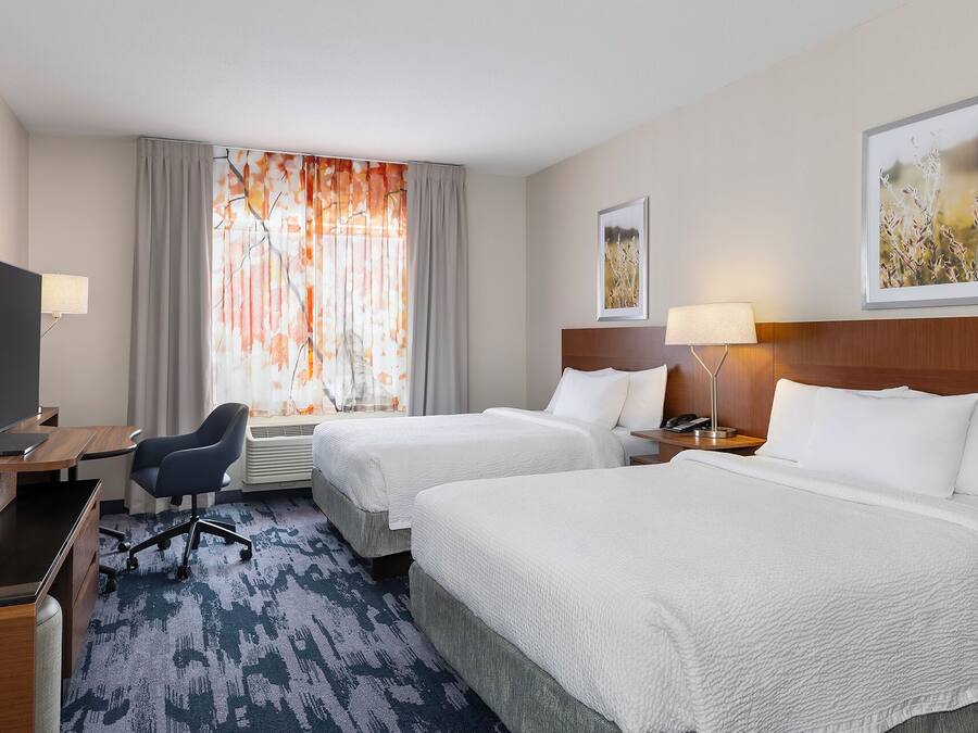 A hotel room with two beds, a desk with a computer, a chair, and a window with curtains.