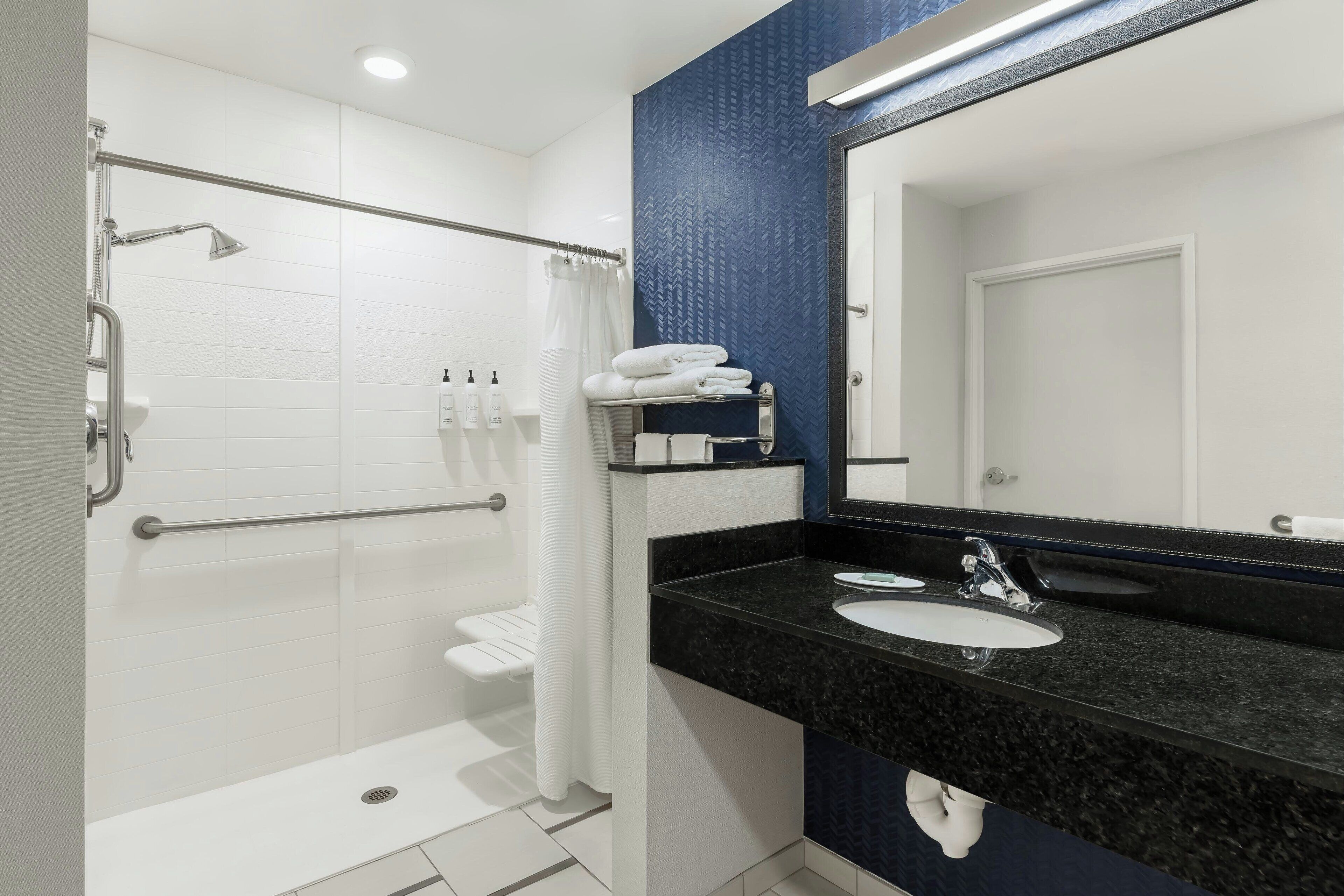 A modern bathroom with a shower, grab bar, white tiles, a black granite countertop, a sink, and a mirror.