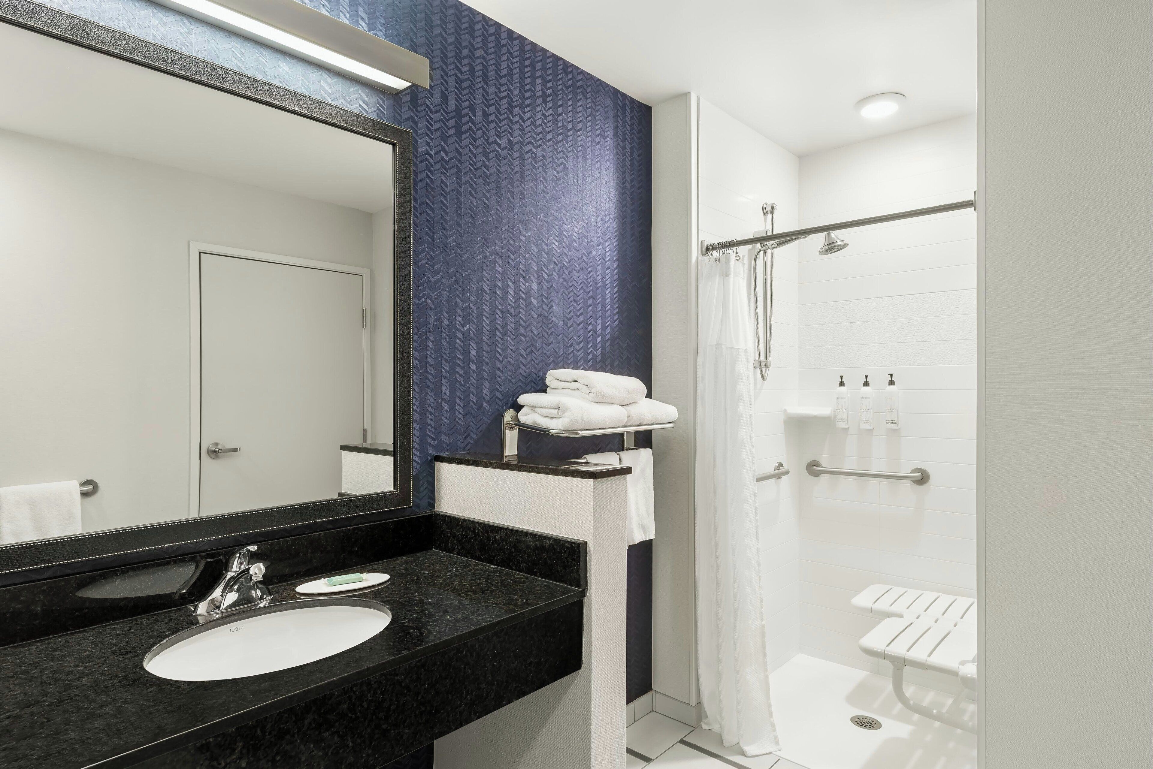 A modern bathroom with a black granite sink, a large mirror, and a walk-in shower with a glass door.