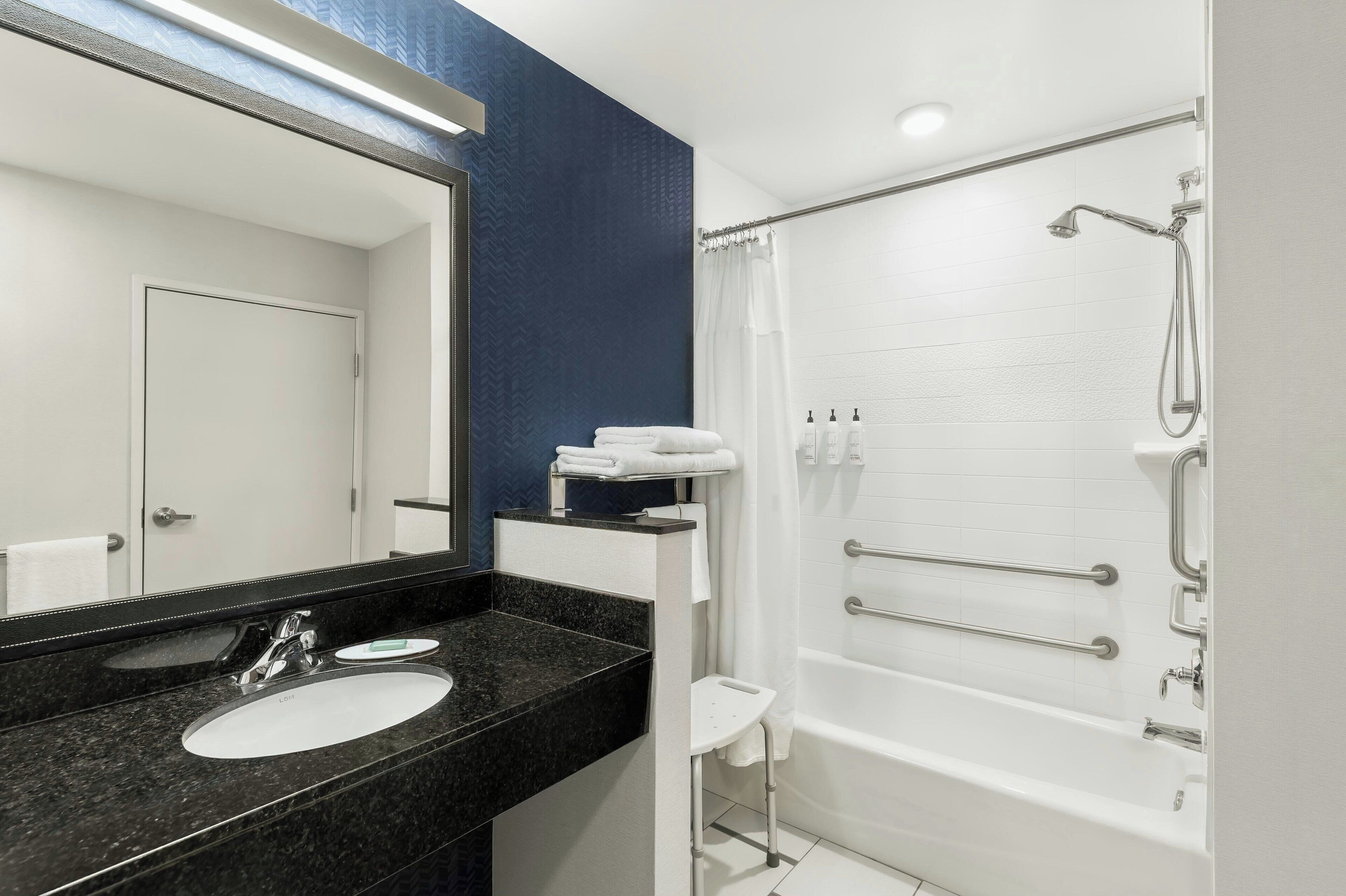 A modern bathroom with a black granite sink, white vanity, and a walk-in shower with grab bars.