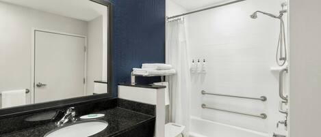 Un baño moderno con un lavabo de granito negro, tocador blanco y ducha a ras de suelo con barras de apoyo.
