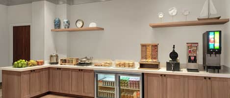 A modern kitchen area with a built-in refrigerator, a coffee machine, and various food items on the counter.