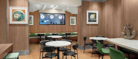 A restaurant with round tables and green chairs, wooden walls, and framed artwork.
