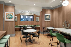 A restaurant with round tables and green chairs, wooden walls, and framed artwork.