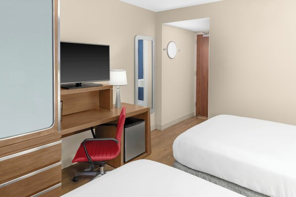 A hotel room with a bed, a desk with a chair, a television, and a mirror.