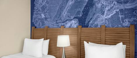 A hotel room with two beds, a wooden headboard, a nightstand with a lamp, and a large map mural on the wall.
