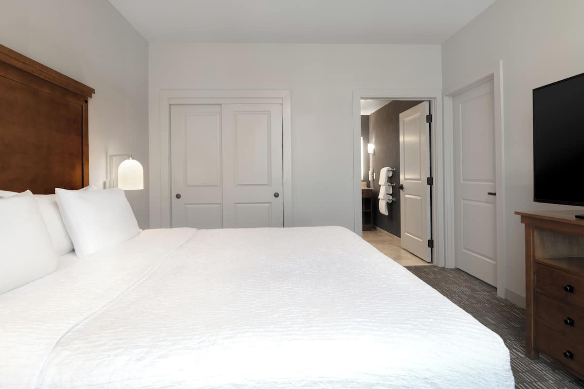 Hotelkamer met een groot bed, een houten hoofdbord, een televisie op een houten standaard, en een badkamer zichtbaar door een open deur.