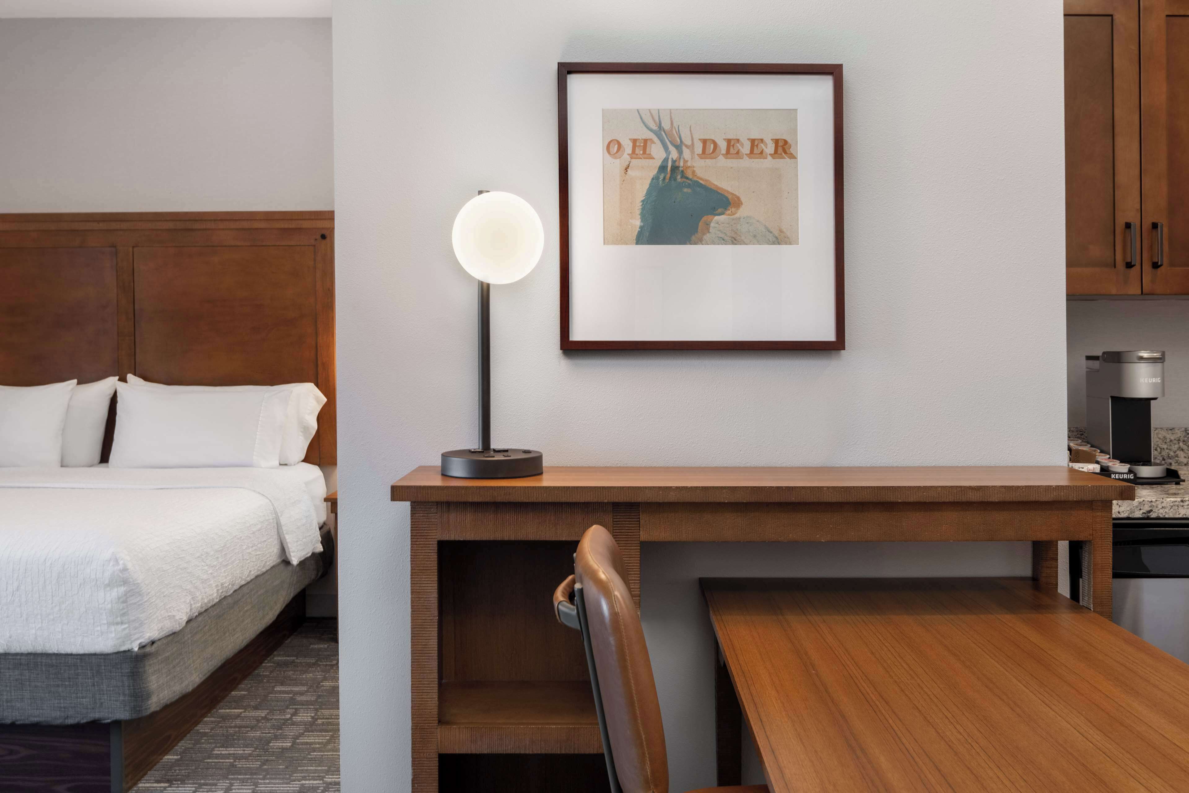 A hotel room with a bed, a desk, a framed picture, a lamp, and a coffee machine.