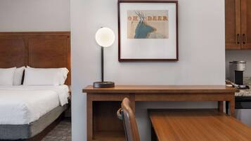 A hotel room with a bed, a desk, a framed picture, a lamp, and a coffee machine.