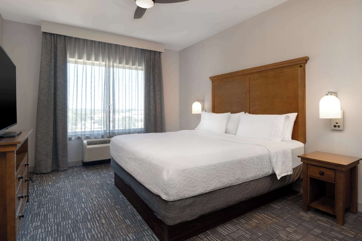 Een hotelkamer met een groot bed, een houten hoofdeinde, een nachtkastje, een televisie en een raam met gordijnen.