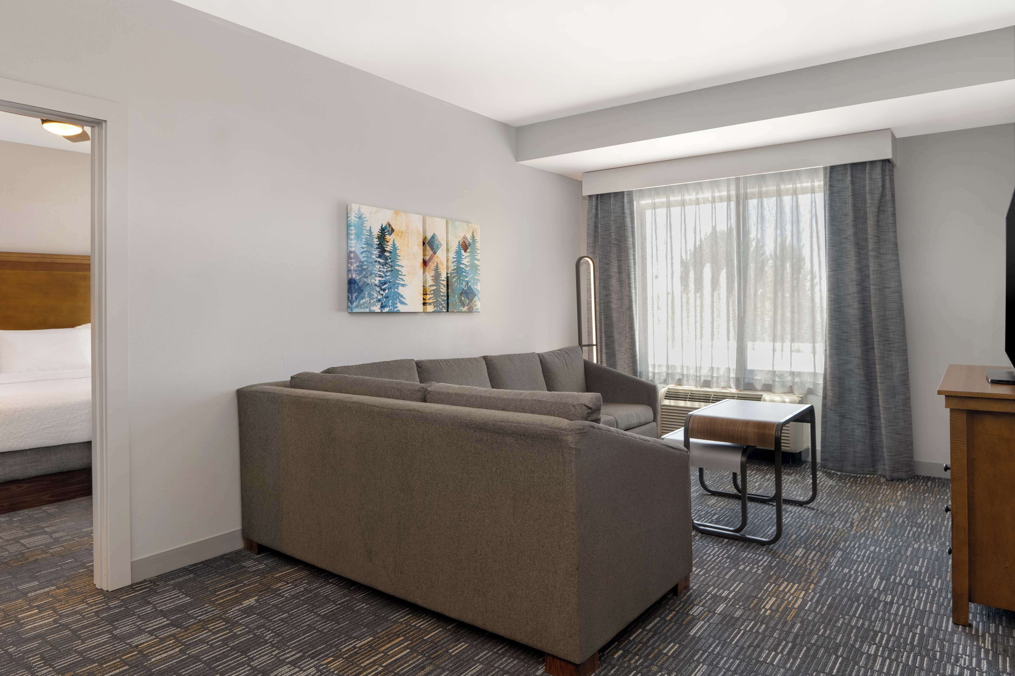 A modern hotel room with a sofa, a small table, a TV, and artwork on the wall.