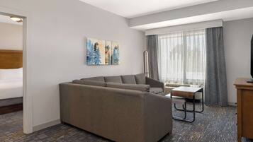 A modern hotel room with a sofa, a small table, a TV, and artwork on the wall.