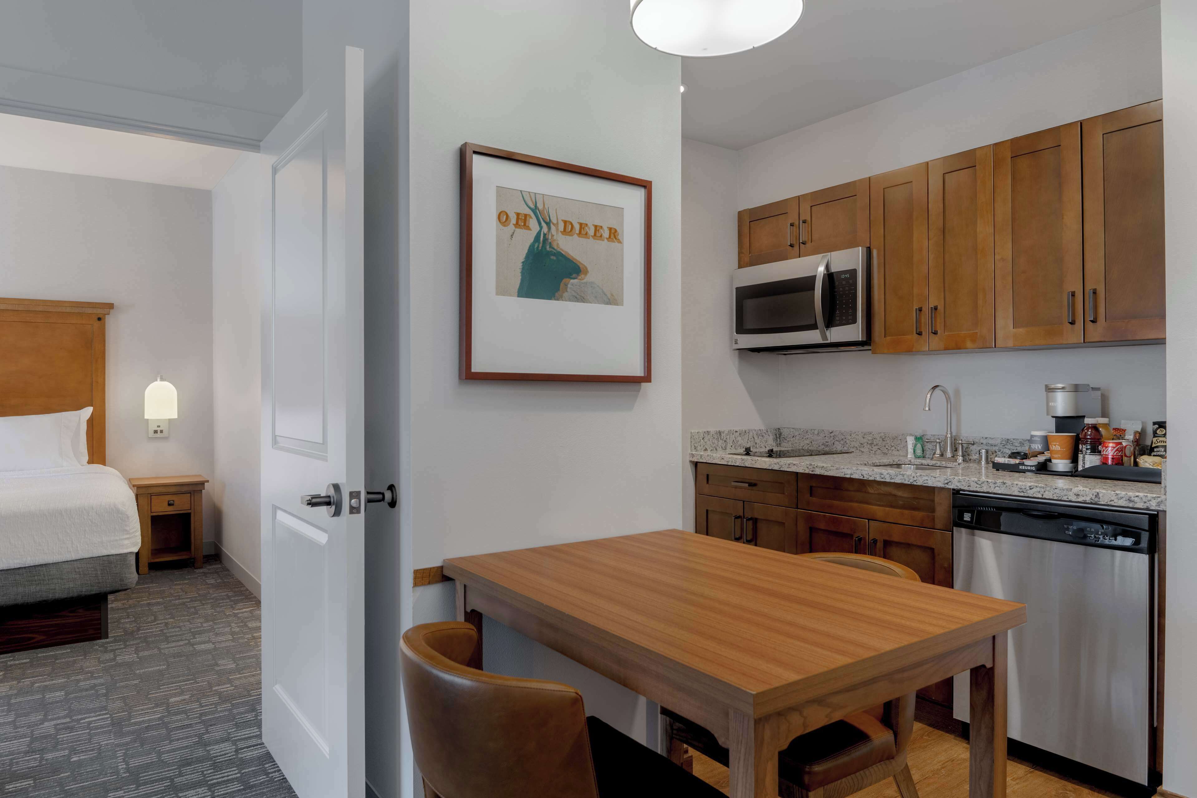 Une chambre d’hôtel comprenant un lit, une table à manger en bois, une cuisine avec des placards en bois, un four à micro-ondes et un lave-vaisselle.