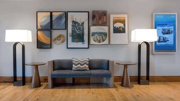 A modern lobby with a grey sofa, two floor lamps, and framed artwork on the wall.