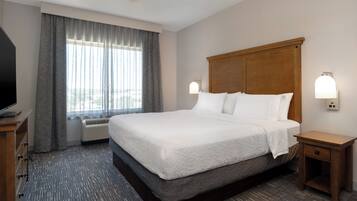 A hotel room with a large bed, a flat-screen TV, a wooden nightstand, and a window with curtains.