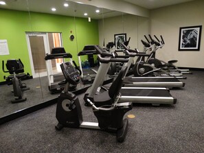 A gym with multiple cardio machines, a mirrored wall, and a green accent wall. - Holiday Inn Covington by IHG (Covington)