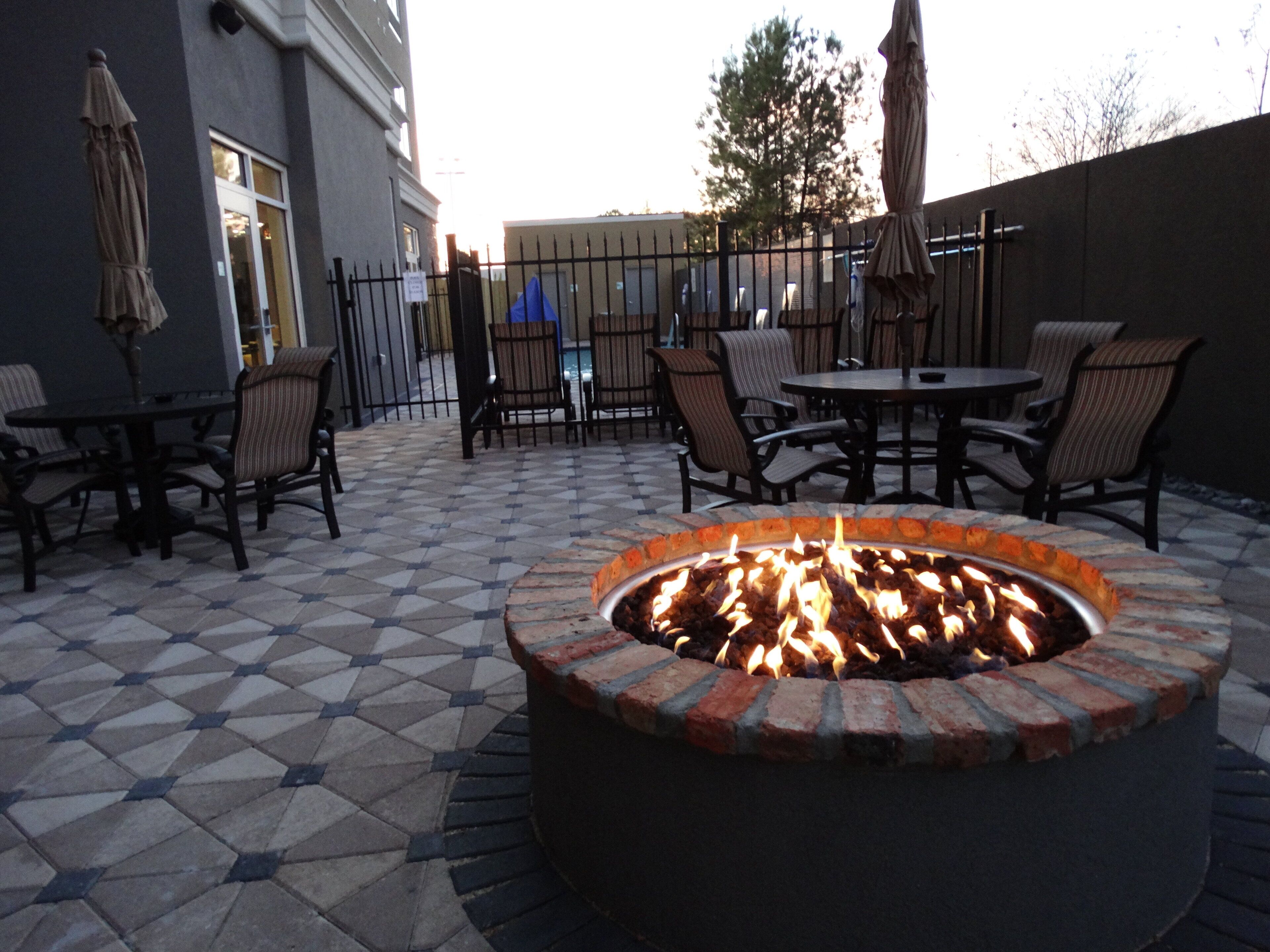 An outdoor patio with a fire pit, seating area, and a building in the background.