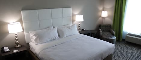 Une chambre d’hôtel avec un grand lit, deux tables de chevet, une chaise, une lampe et une fenêtre avec des rideaux.