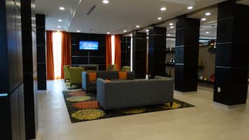 A modern living room with a sofa, chairs, a flat-screen TV, and a patterned rug.