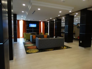 A modern living room with a sofa, chairs, a flat-screen TV, and a patterned rug.
