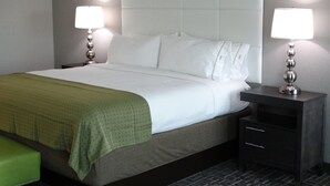 A neatly made bed with white linens and a green blanket, flanked by two bedside tables with lamps, in a room with a simple, clean design. - Holiday Inn Covington by IHG (Covington)