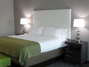 A neatly made bed with white linens and a green blanket, flanked by two bedside tables with lamps, in a room with a simple, clean design. - Holiday Inn Covington by IHG (Covington)