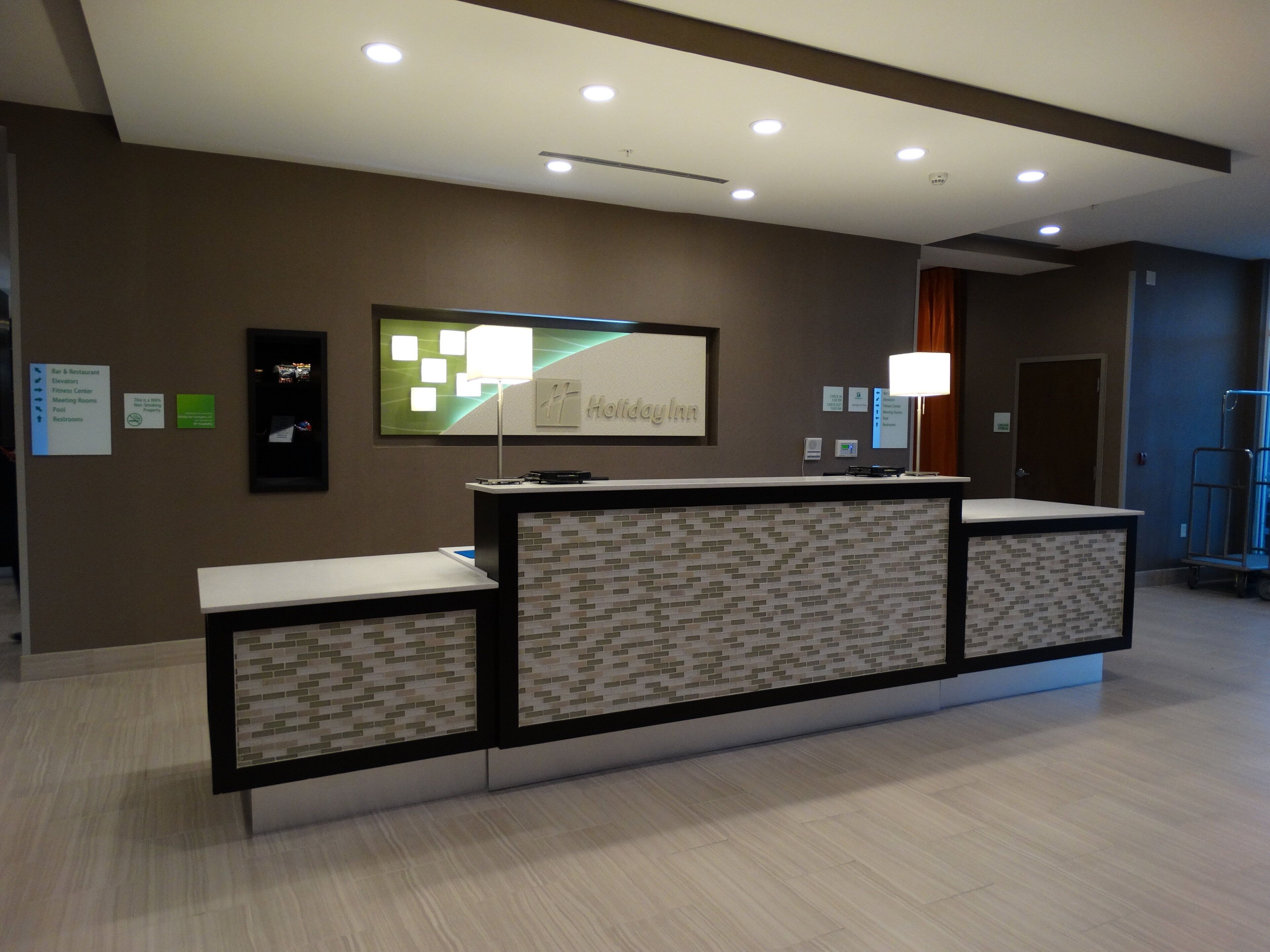 A hotel reception desk with a digital screen, a framed sign, and a wall-mounted information board.