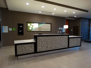A hotel reception desk with a digital screen, a framed sign, and a wall-mounted information board. - Holiday Inn Covington by IHG (Covington)