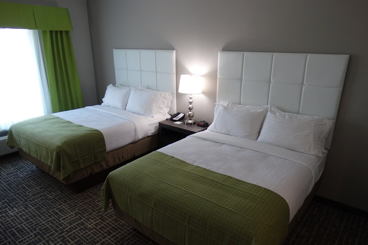 Two adjacent hotel beds with headboards, a bedside table with a lamp, and a patterned carpet.