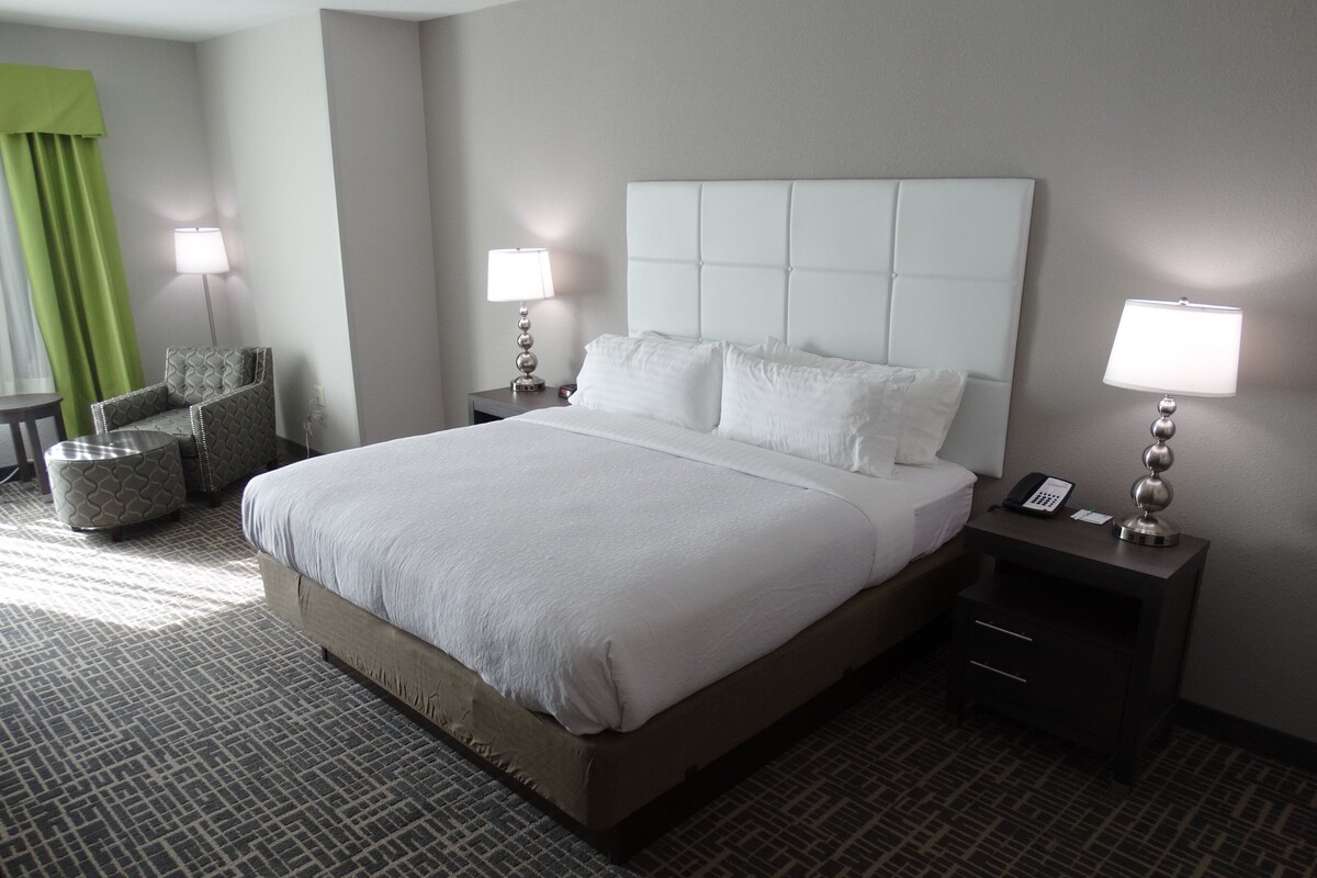 A hotel room with a large bed, two bedside tables, a chair, and a lamp.