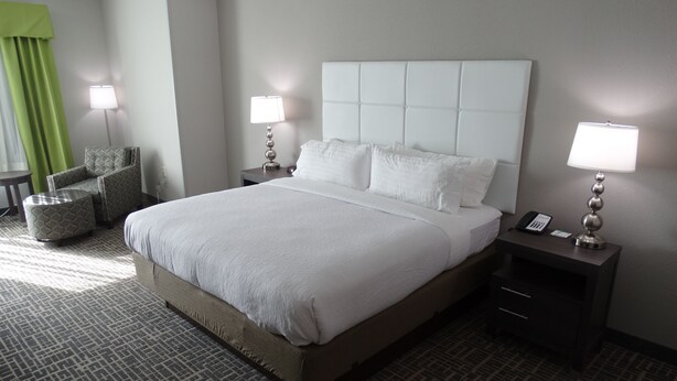 A hotel room with a large bed, two bedside tables with lamps, a chair, and a patterned carpet. - Holiday Inn Covington by IHG (Covington)