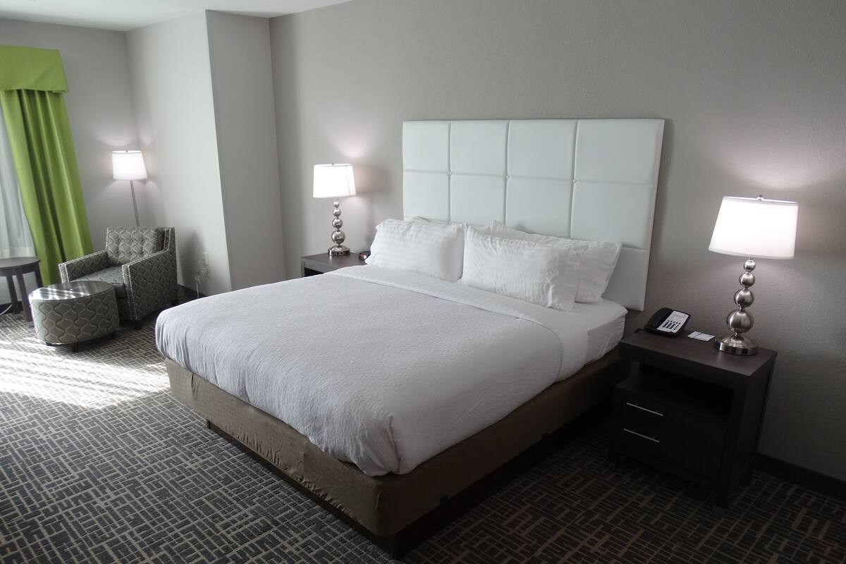 A hotel room with a large bed, two bedside tables with lamps, a chair, and a patterned carpet.