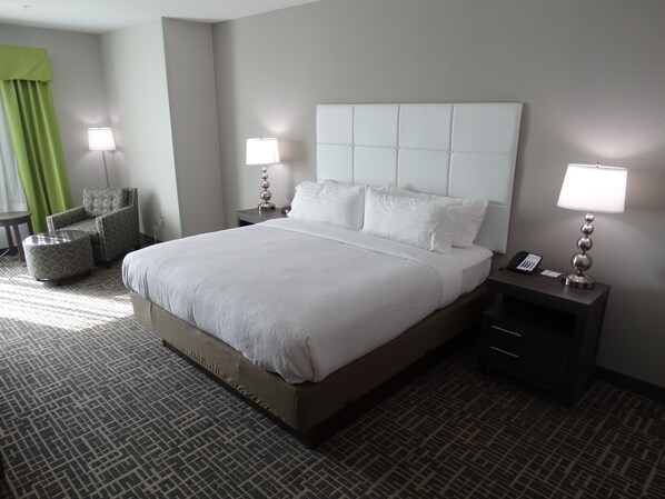 A hotel room with a large bed, two bedside tables with lamps, a chair, and a patterned carpet. - Holiday Inn Covington by IHG (Covington)