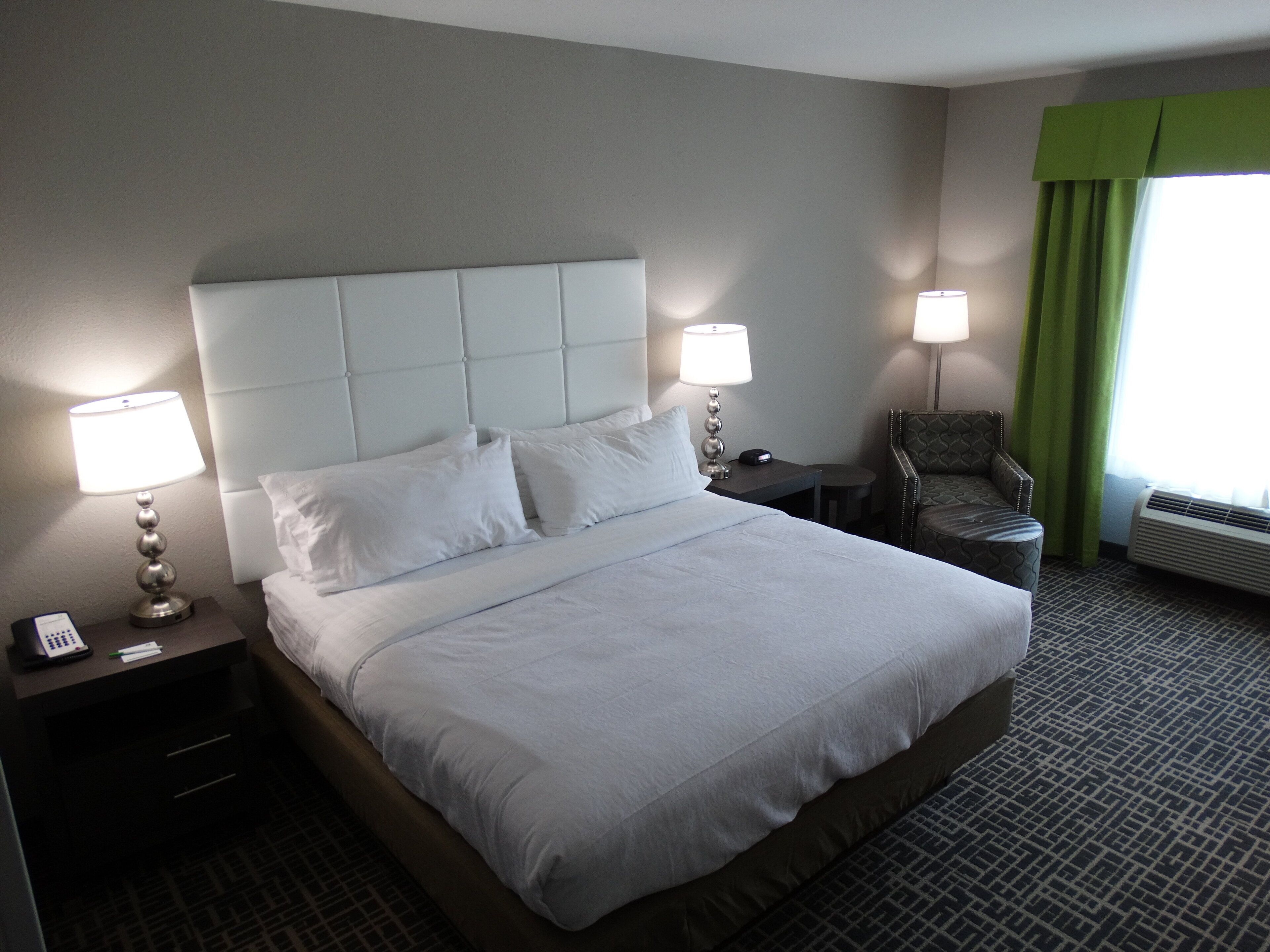 A hotel room with a large bed, two bedside tables with lamps, a chair, and a window with curtains.