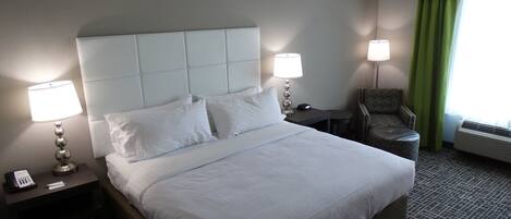 A hotel room with a large bed, two bedside tables with lamps, a chair, and a window with curtains.