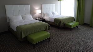 A hotel room with two beds, a nightstand, a lamp, and a green bench. - Holiday Inn Covington by IHG (Covington)