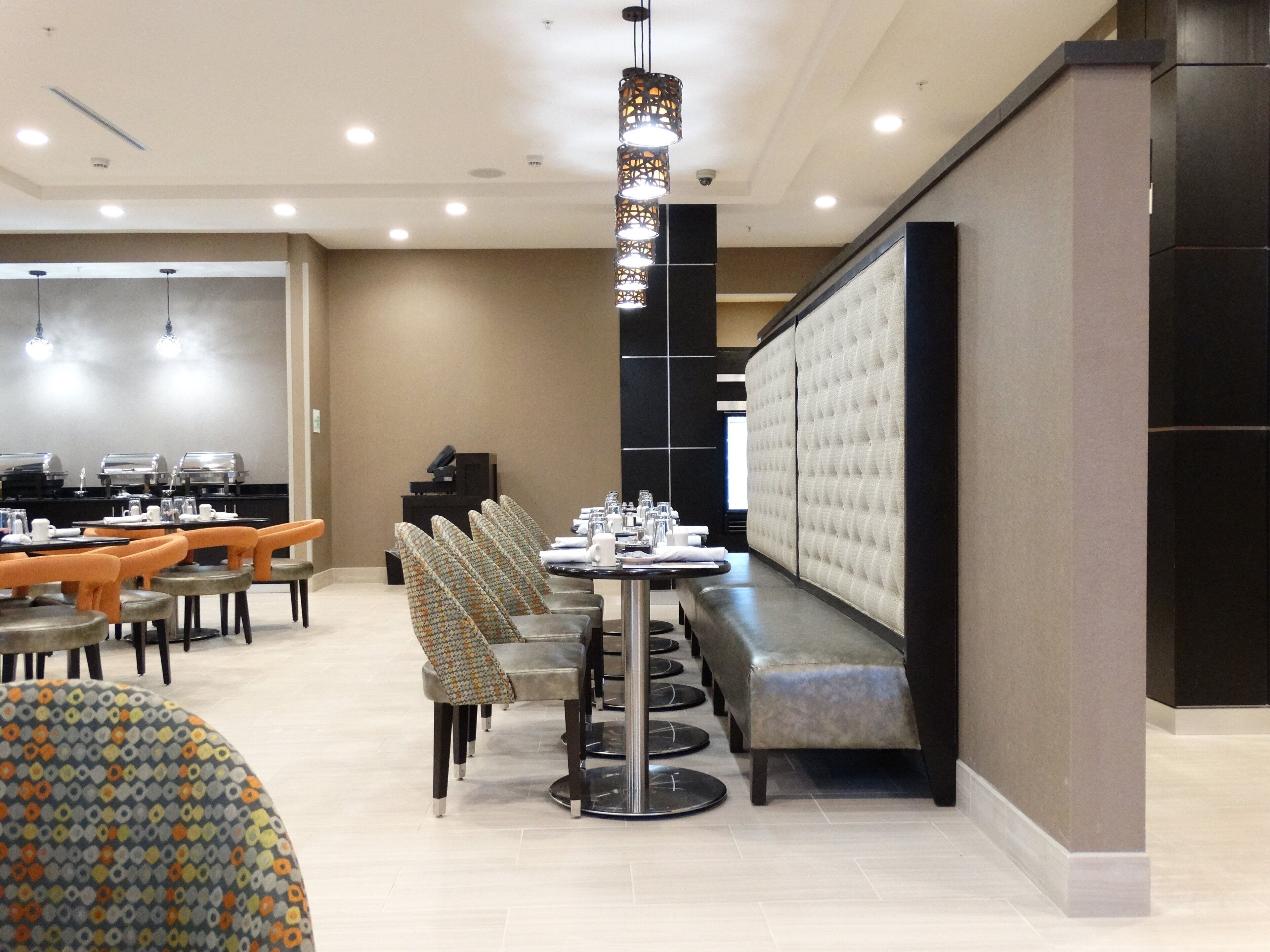 A modern hotel dining area with a long table, multiple chairs, and a cushioned bench.